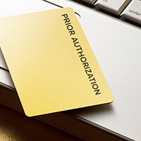 Gold card on top of laptop computer that says Prior Authorization