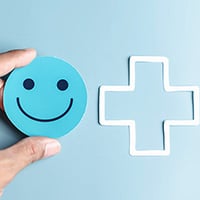 Image of person holding a smiley face with a health cross next to it on a blue background